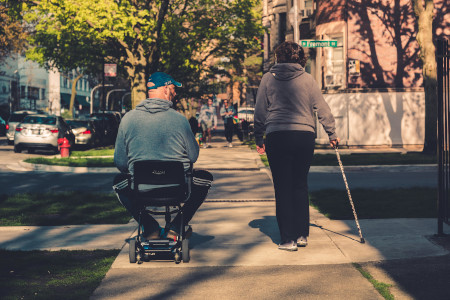 A wheelchair user and a woman using a cane side by side