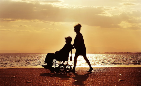 A wheelchair user is pushed by a friend at the beach