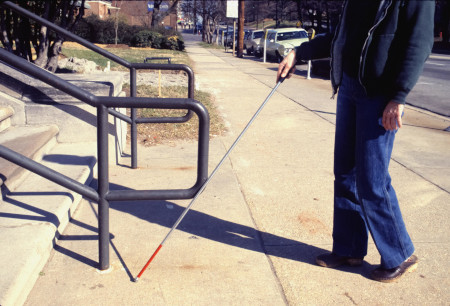 A blind person using a cane is walking towards a staircase