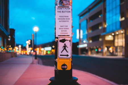 An accessible pedestrian signal installed with a pushbutton. The sign on the pole says: "Don’t push the button. Pedestrian crossing now automated. Wait for WALK signal before crossing".